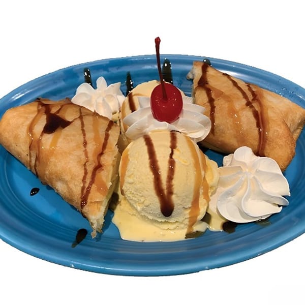 Two fried pastries with vanilla ice cream, whipped cream, caramel drizzle, and a cherry on a blue plate.